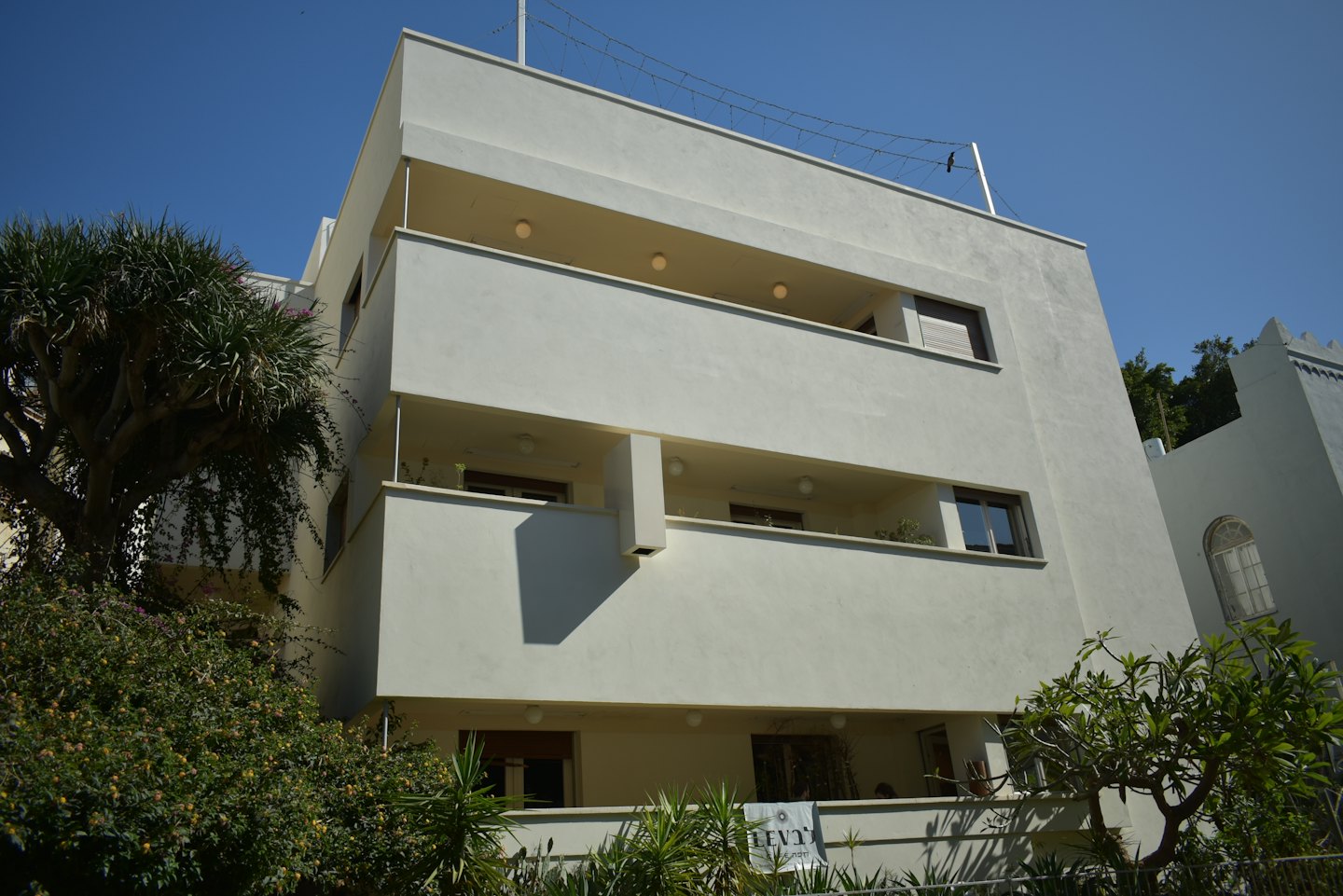 Palazzo modernista con balconi a terrazze e verde lussureggiante.